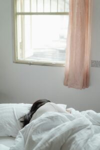 A woman peacefully sleeping in a sunlit bedroom with soft bedding and curtains.