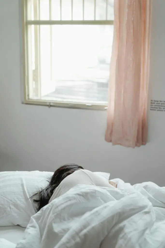 A woman peacefully sleeping in a sunlit bedroom with soft bedding and curtains.