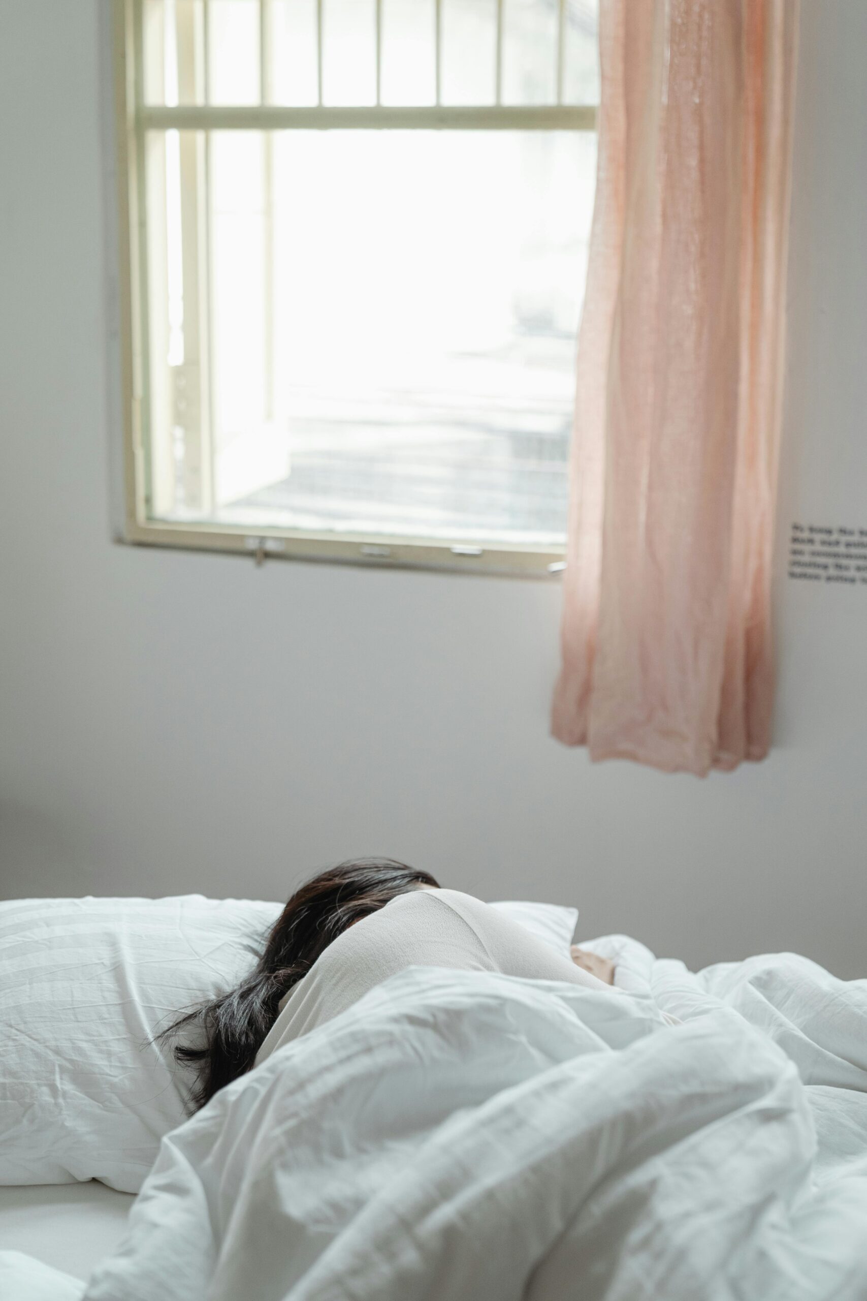 A woman peacefully sleeping in a sunlit bedroom with soft bedding and curtains.