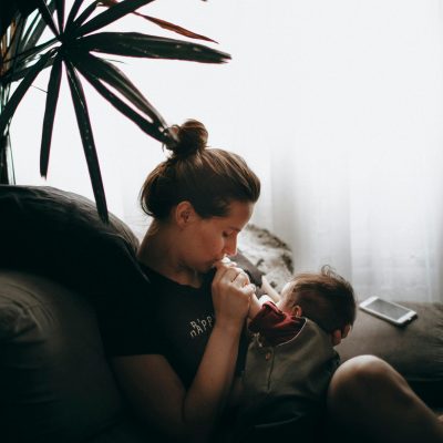 Side view of caring mother sitting on comfortable sofa with little son while cuddling in light living room at home